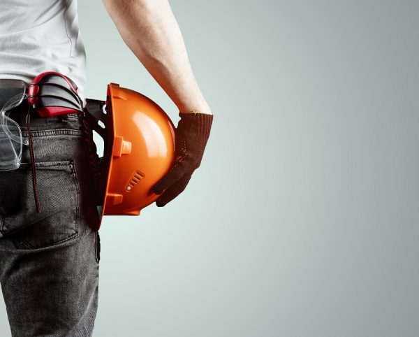 The builder, the architect holds in his hand a construction helmet on a light background, a tape measure.