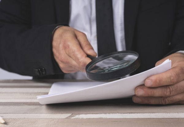 Close-up of the hands of a Businessman looking through a magnifying glass for documents